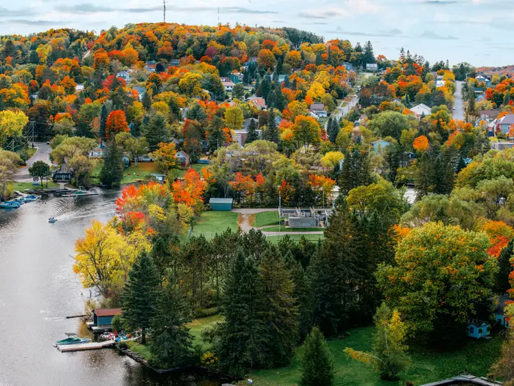 Luftaufnahme von Huntsville, Ontario, mit buntem Herbstlaub rund um den Fluss und der zwischen sanften Hügeln eingebetteten Stadt.