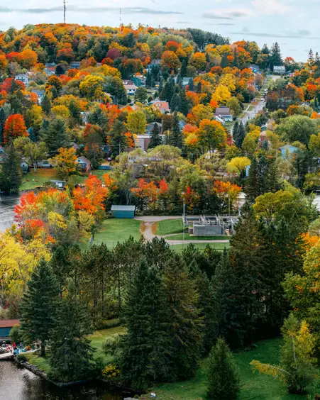 Aerial view of Huntsville, Ontario, with colourful fall foliage surrounding the river and town nestled among rolling hills.