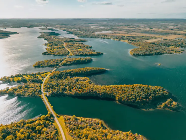 Route sinueuse de Long Sault Parkway traversant des îles boisées sous le soleil, avec les eaux scintillantes du lac s'étendant à perte de vue.