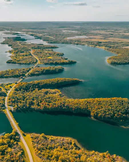 Die kurvenreiche Straße des Long Sault Parkway führt an einem sonnigen Tag über bewaldete Inseln, während sich das schimmernde Wasser eines Sees durch die Landschaft erstreckt.