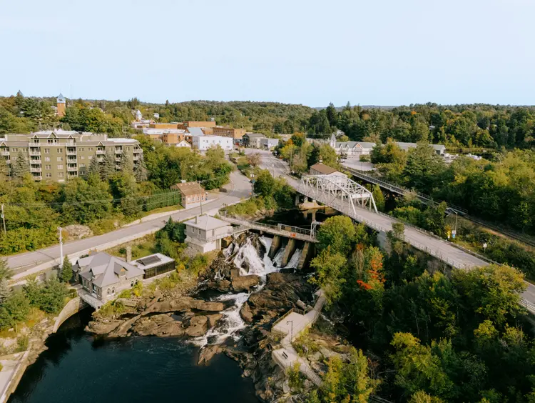 Luftaufnahme von Bracebridge mit einer malerischen Brücke, Wasserfällen und einer Mischung aus Waldgebieten und Stadtgebäuden.