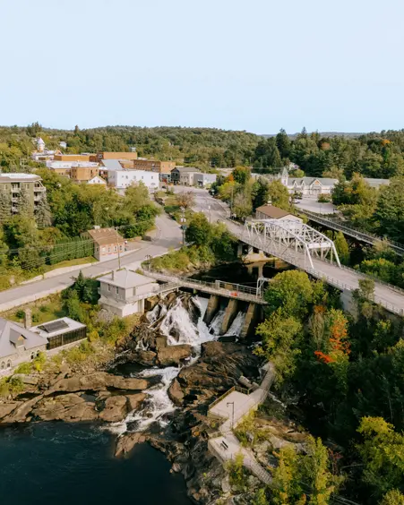 Aerial view of Bracebridge with a scenic bridge, waterfalls, and a mix of forested areas and town buildings.