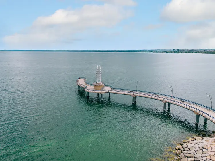 Der Brant Street Pier wölbt sich unter einem bewölkten Himmel in das türkisfarbene Wasser des Ontariosees, während Besucher am Pier entlang spazieren.