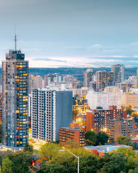Die Skyline von Hamilton, Ontario, leuchtet zur blauen Stunde, mit Hochhäusern und Bürotürmen, die sich vor einem Abendhimmel abheben.