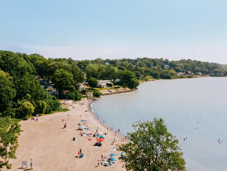 Des amateurs de plage le long du rivage sablonneux du lac Érié à Port Stanley, des vagues calmes et des chalets nichés parmi des arbres luxuriants.