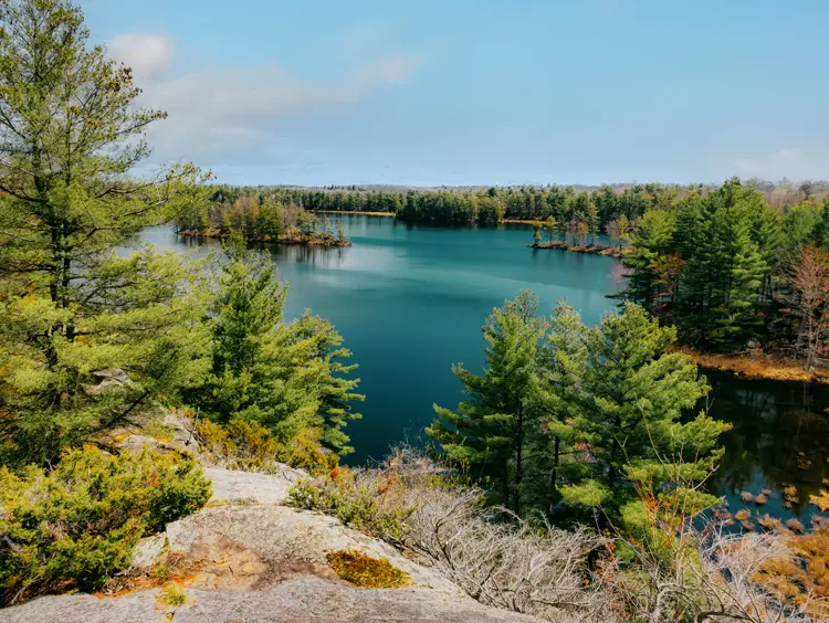 Vue sur le lac entouré d'un relief rocheux et d'une dense forêt de pins au parc provincial Frontenac, par une journée printanière un peu nuageuse.
