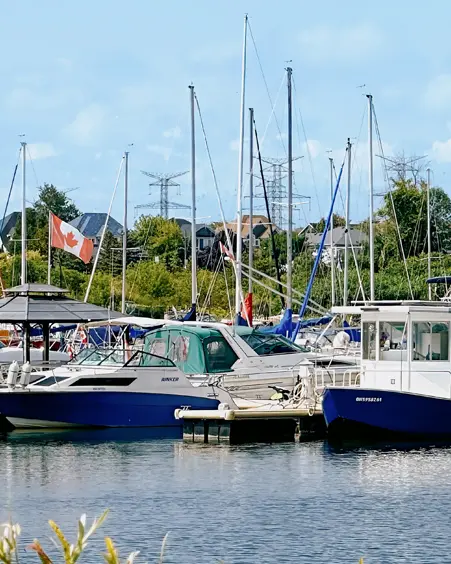 Barcos atracados en un puerto deportivo en Clarington, Ontario, con mástiles de veleros elevándose sobre el agua y una bandera canadiense ondeando en la brisa.