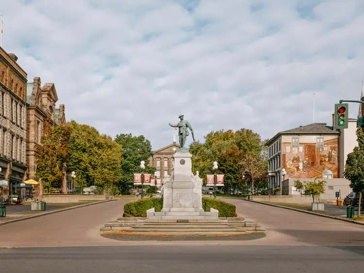 Centre-ville historique de Brockville avec un monument commémoratif central, des bâtiments patrimoniaux et des rues bordées d'arbres sous les nuages.