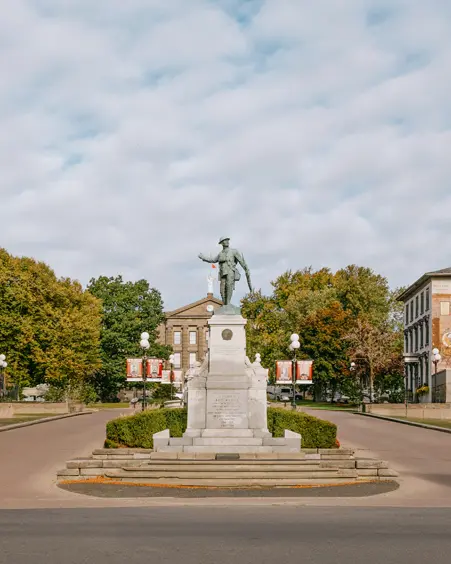 Centre-ville historique de Brockville avec un monument commémoratif central, des bâtiments patrimoniaux et des rues bordées d'arbres sous les nuages.