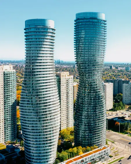 Aerial view of the Absolute World Complex in Mississauga, with the curving, modern twin towers rising above surrounding high-rises on a clear day.