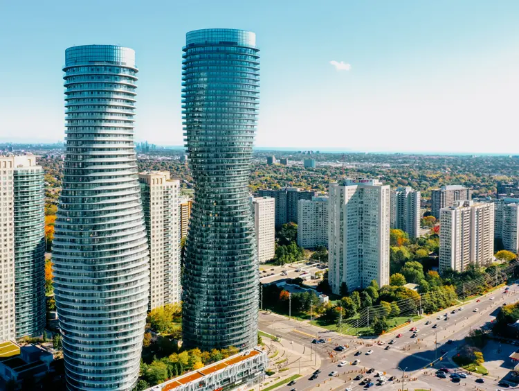 Vue aérienne des tours jumelles modernes du complexe Absolute World à Mississauga qui surplombent les gratte-ciel environnants sous un ciel bleu.