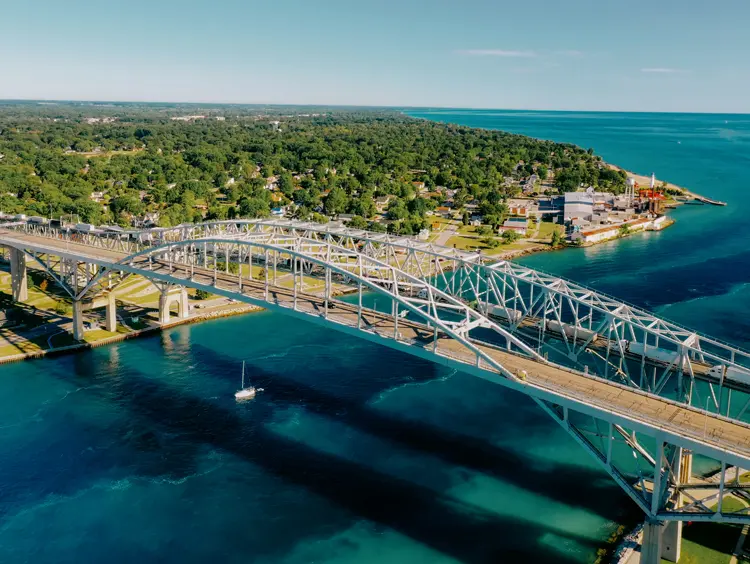 Vue aérienne du pont Blue Water enjambant la rivière Sainte-Claire d’un bleu éclatant et reliant Sarnia et Port Huron, avec une rive verdoyante.