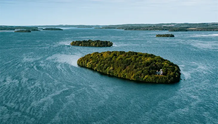 Luftaufnahme von Cobourg im Rice Lake mit einer üppigen, baumbedeckten Insel, umgeben von ruhigem blauen Wasser und kleineren Inseln in der Ferne.