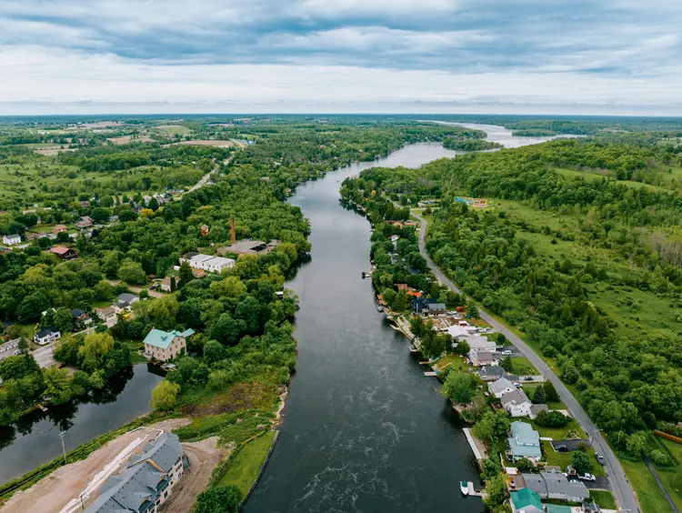 Aerial view of Hastings, Ontario, showing a winding river lined with homes and trees, stretching through a lush, green rural landscape.