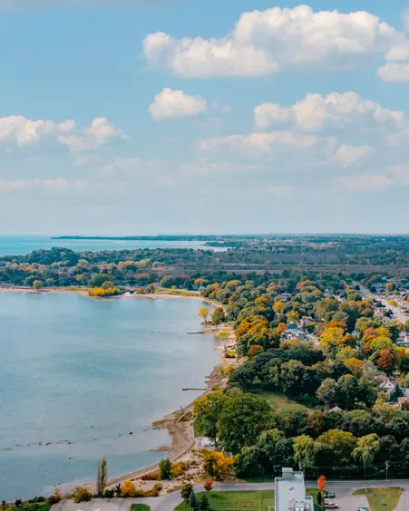  Luftaufnahme des H.H. Knoll Lakeview Park und der Uferlinie des Eriesees in Port Colborne mit bunten Herbstbäumen und einem hellen, wolkenverhangenen Himmel.