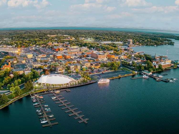 Vista aérea de Kenora, Ontario, al atardecer, con barcos atracados a lo largo de la costa y suaves nubes de color púrpura sobre el lago de los Bosques.