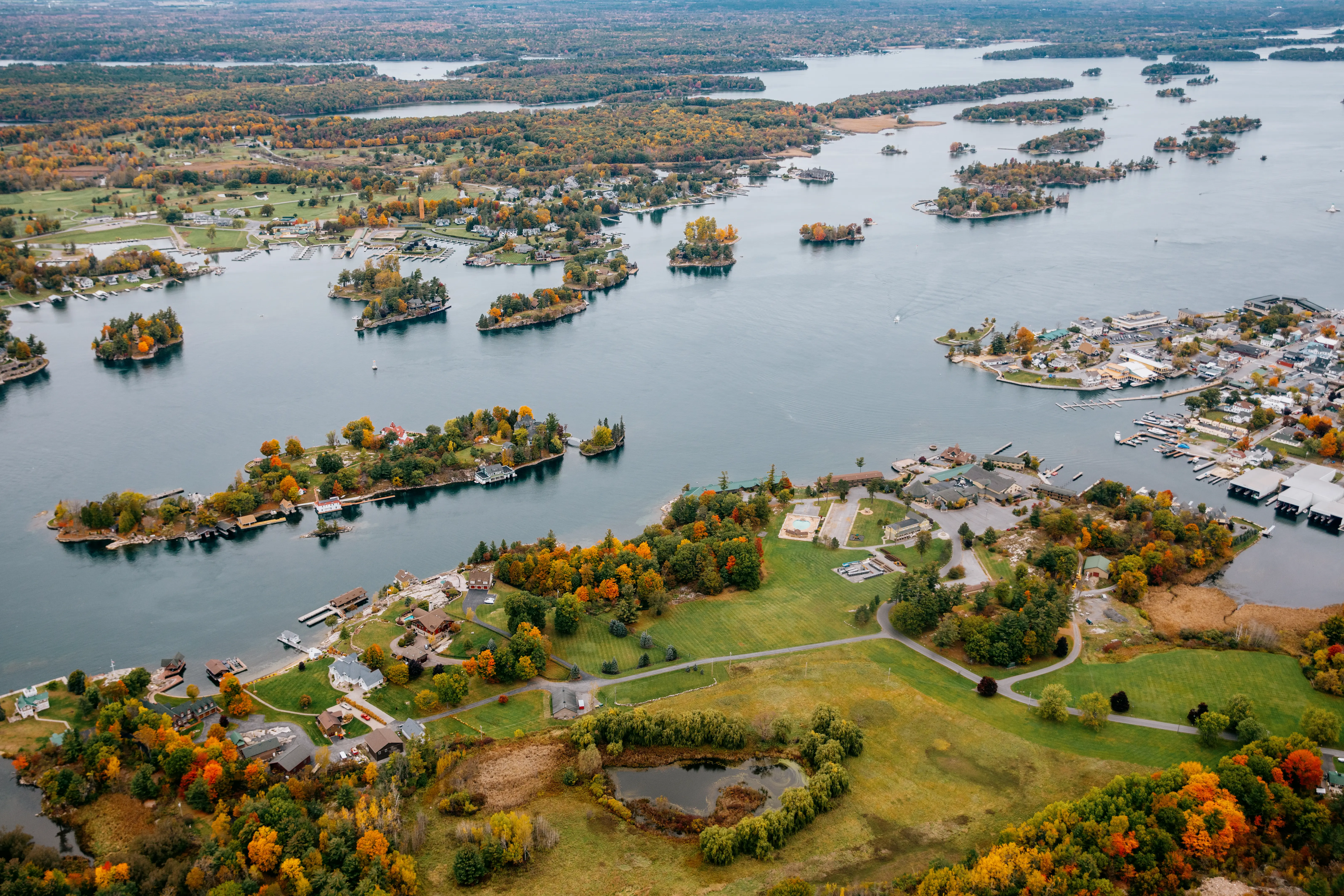 Vue aérienne de la région des Mille Îles, parsemée de petites îles boisées et de maisons riveraines, sous un ciel d’automne couvert.