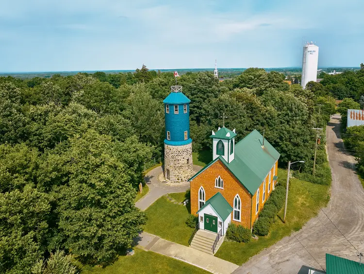 Vue aérienne de la Tour Higginson et de l’église anglicane St. John the Apostle, à Vankleek Hill, entourées d’arbres verts, un jour d’été.
