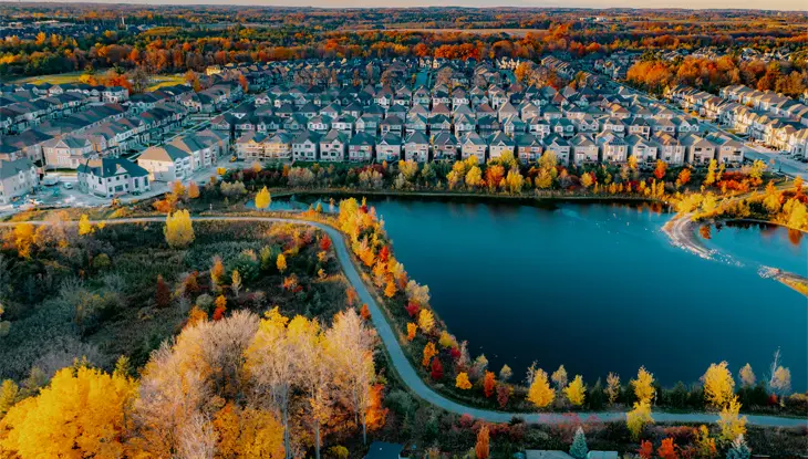 Luftaufnahme eines Vororts von Woodbridge mit Reihen ordentlich aufgereihter Häuser, einem kleinen See, gewundenen Pfaden und bunten Herbstbäumen an einem Herbsttag.