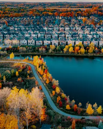 Aerial view of a Woodbridge suburb with rows of neatly aligned houses, a small lake, winding trails and colourful autumn trees on a fall day.