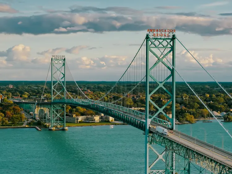 Vue aérienne du pont Ambassador s’étendant sur des eaux turquoise et reliant Windsor, en Ontario, aux États-Unis, sous un ciel couchant.