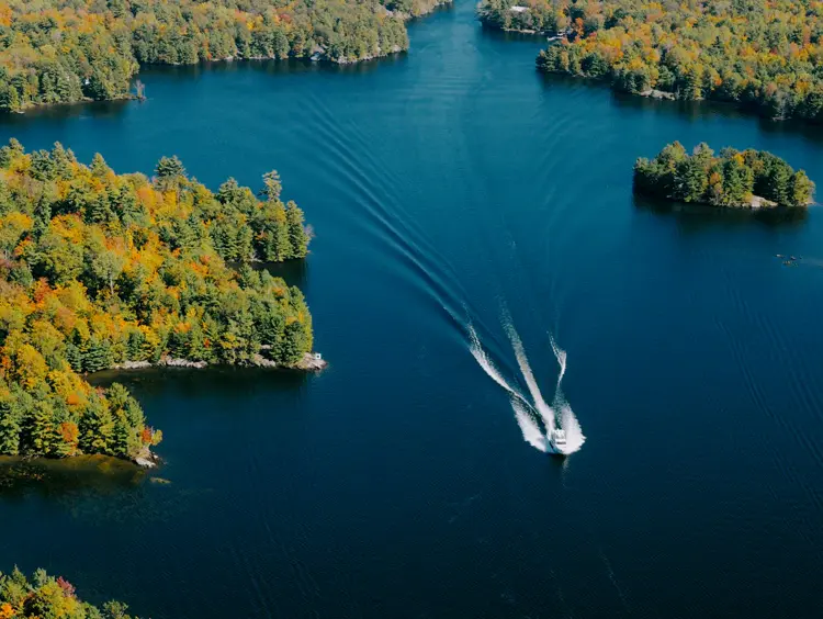 Dos barcos navegando por un lago azul dejando rastros blancos, rodeados de una costa boscosa en Orillia y Lake Country.