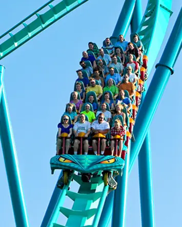 Un groupe de personnes à bord de montagnes russes sous un ciel bleu d’été.