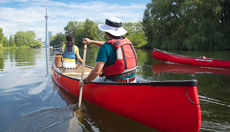 トロントの港湾沿いにあるCNタワーに向かって赤いカヌーを漕ぐ2人。
