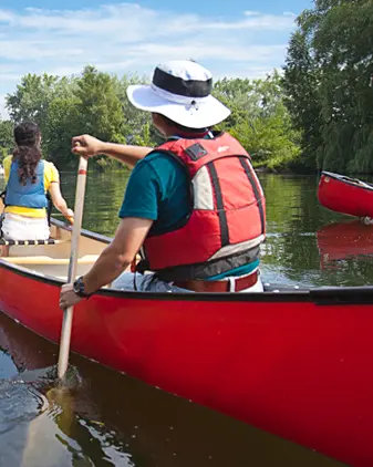 トロントの港湾沿いにあるCNタワーに向かって赤いカヌーを漕ぐ2人。