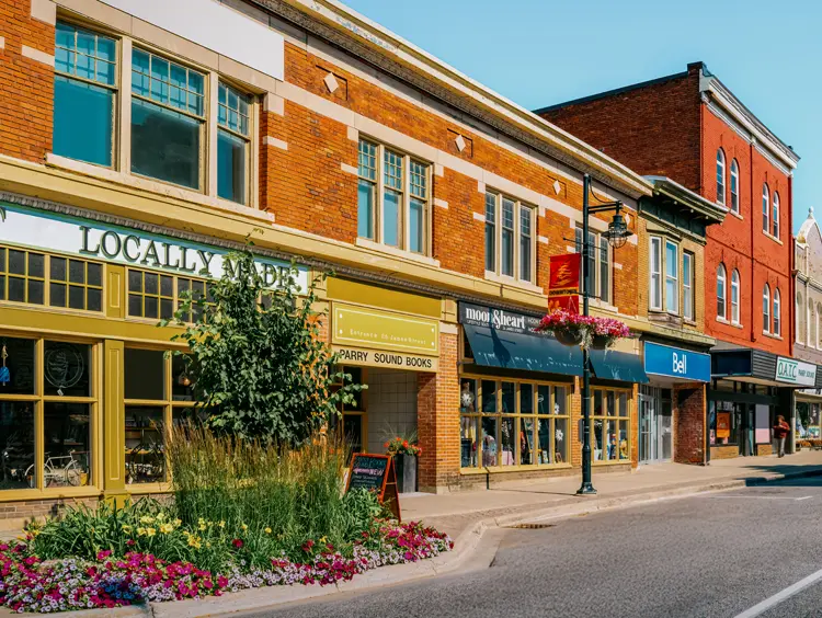 Bunte historische Geschäfte in der Innenstadt von Parry Sound, mit hellen Blumenkästen entlang des Bürgersteigs und hängenden Körben an einem klaren Sommertag.