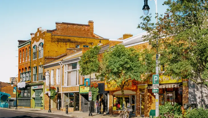 Colourful historic storefronts in downtown St. Catharines on a sunny summer day, with trees and flower beds along the sidewalk.