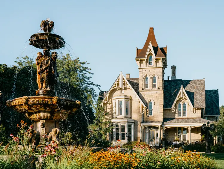 Manoir victorien historique avec fontaine ornée, entouré de jardins, à Elm Hurst Inn & Spa, à Ingersoll, un jour ensoleillé.