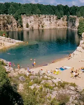 Sandy beach with visitors relaxing and swimming, surrounded by cliffs at Elora Quarry Conservation Area.