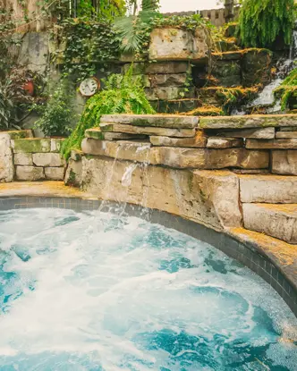 A bubbling hot tub at Pillar and Post Inn & Spa in Niagara-on-the-Lake with a small waterfall flowing into it, surrounded by stone walls and lush greenery.