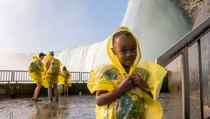 Touristen, darunter ein junges Mädchen, tragen Ponchos, um sich vor dem Nebel der Niagarafälle zu schützen.