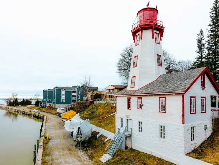 Faro octogonal blanco y rojo de Kincardine junto a la costa del lago Huron en un día nublado, con barcos estacionados cerca.