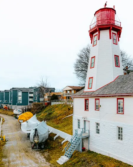 Le phare octogonal blanc et rouge de Kincardine, sur la rive du lac Huron, par une journée nuageuse, avec des bateaux entreposés à proximité.