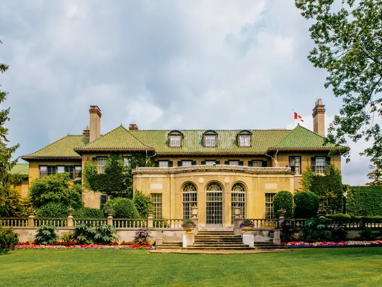 Rückansicht des Herrenhauses Parkwood Estate mit seiner prächtigen Steinfassade, Bogenfenstern, einem Gründach und gepflegten Gärten unter einem bewölkten Sommerhimmel.