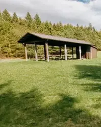 A grassy field with a wooden shelter and picnic tables, surrounded by trees at Souls Path Retreats in Blackstock, Ontario. 