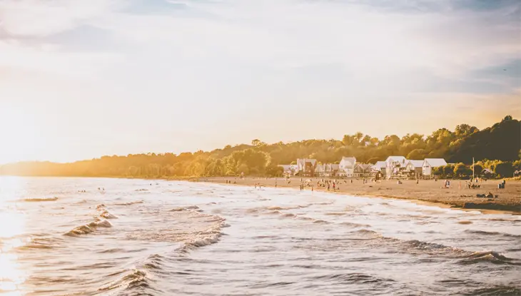 Vista de la playa de Port Stanley al atardecer con suaves olas, gente disfrutando de la costa y pintorescas casas que bordean la playa bajo un suave cielo dorado.