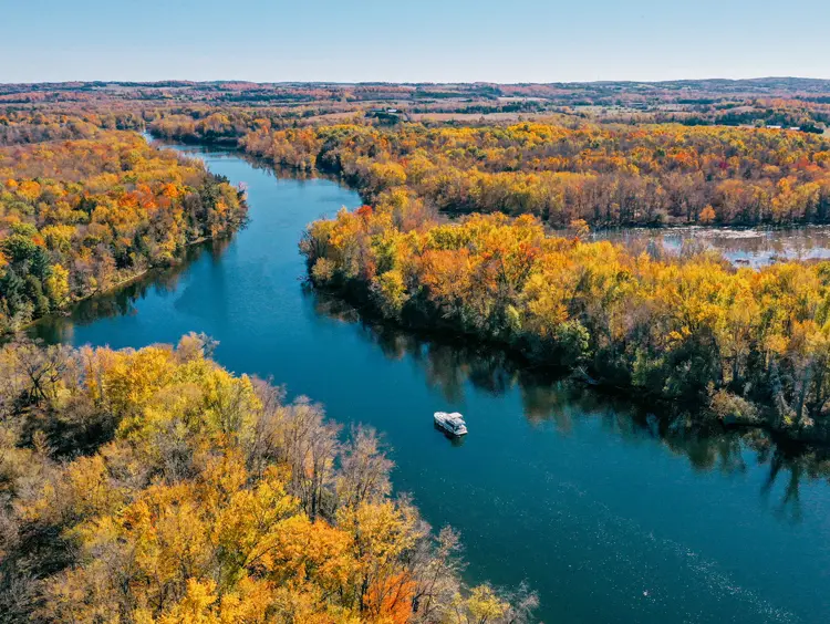 Un río tranquilo que serpentea a través de un paisaje lleno de árboles en Kawartha Lakes, repleto de un vibrante follaje otoñal.