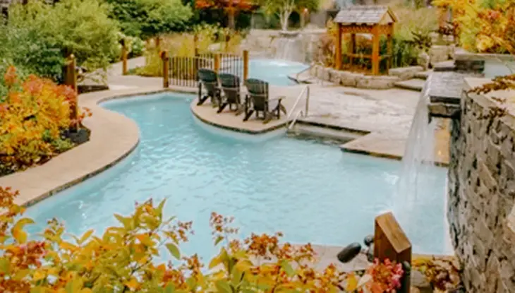 Piscines d’eau chaude et d’eau froide entourées d’arbres d’automne au Scandinave Spa Blue Mountain, avec des chutes et des fauteuils confortables.