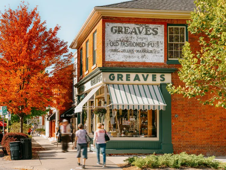 Visitors strolling past Greaves Jams shop and colourful fall trees on the bustling Queen Street in Niagara-on-the-Lake.