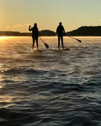 Tres visitantes de Northern Edge Algonquin practican surf de remo en el brillante atardecer del lago Kawawaymog.
