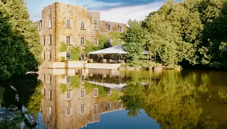 Reflet du bâtiment en pierre du Millcroft Inn & Spa dans les eaux tranquilles d’un étang entouré d’arbres verdoyants.