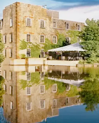 Das denkmalgeschützte Steingebäude des Millcroft Inn & Spa spiegelt sich in einem stillen Teich, umgeben von üppigen grünen Bäumen.