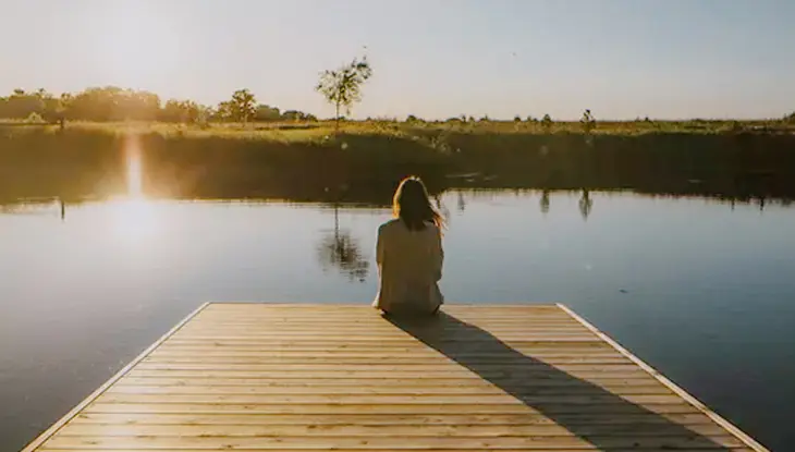 Personne assise au bord d’un quai en bois regardant le soleil se lever sur un lac calme à Luna Homestead, dans l’Ontario rural.