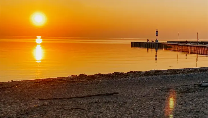  일몰 무렵의 조용한 해변, 빛나는 주황빛 하늘, 그리고 고요한 물 위로 펼쳐진 베이필드 부두.