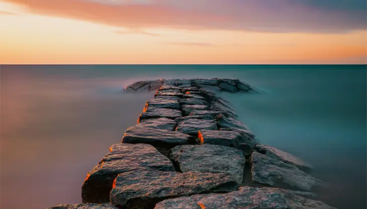 브라이트 그로브의 휴론 호수로 이어지는 돌길 위로 지는 해가 극적인 하늘 아래 빛나고 있습니다.