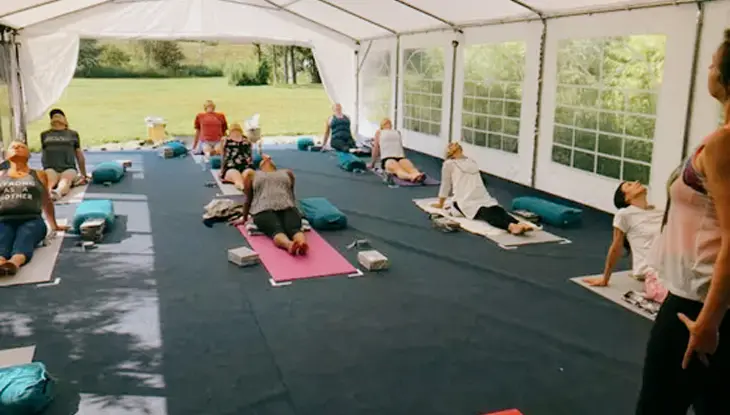 Groupe de neuf participants à une séance de yoga pratiquant des poses sur des tapis à l’intérieur d’une tente au gîte Rising Spirit, à Orono.